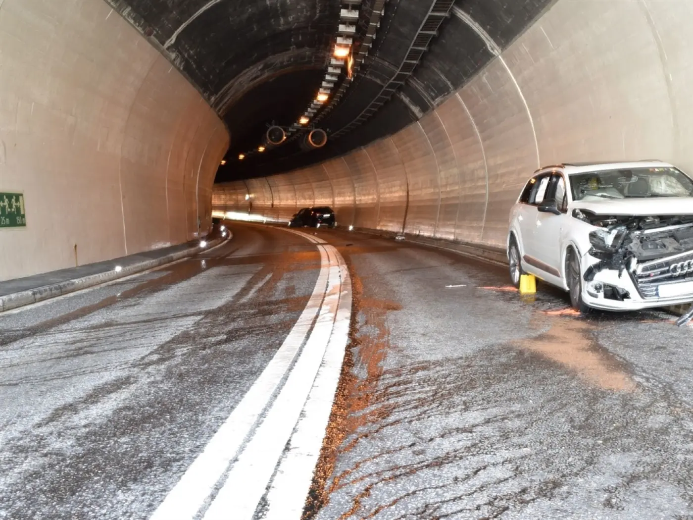 Un tunnel con una strada bagnata. Un'auto bianca è parcheggiata a lato con il muso danneggiato, mentre un'altra auto si intravede più lontano.