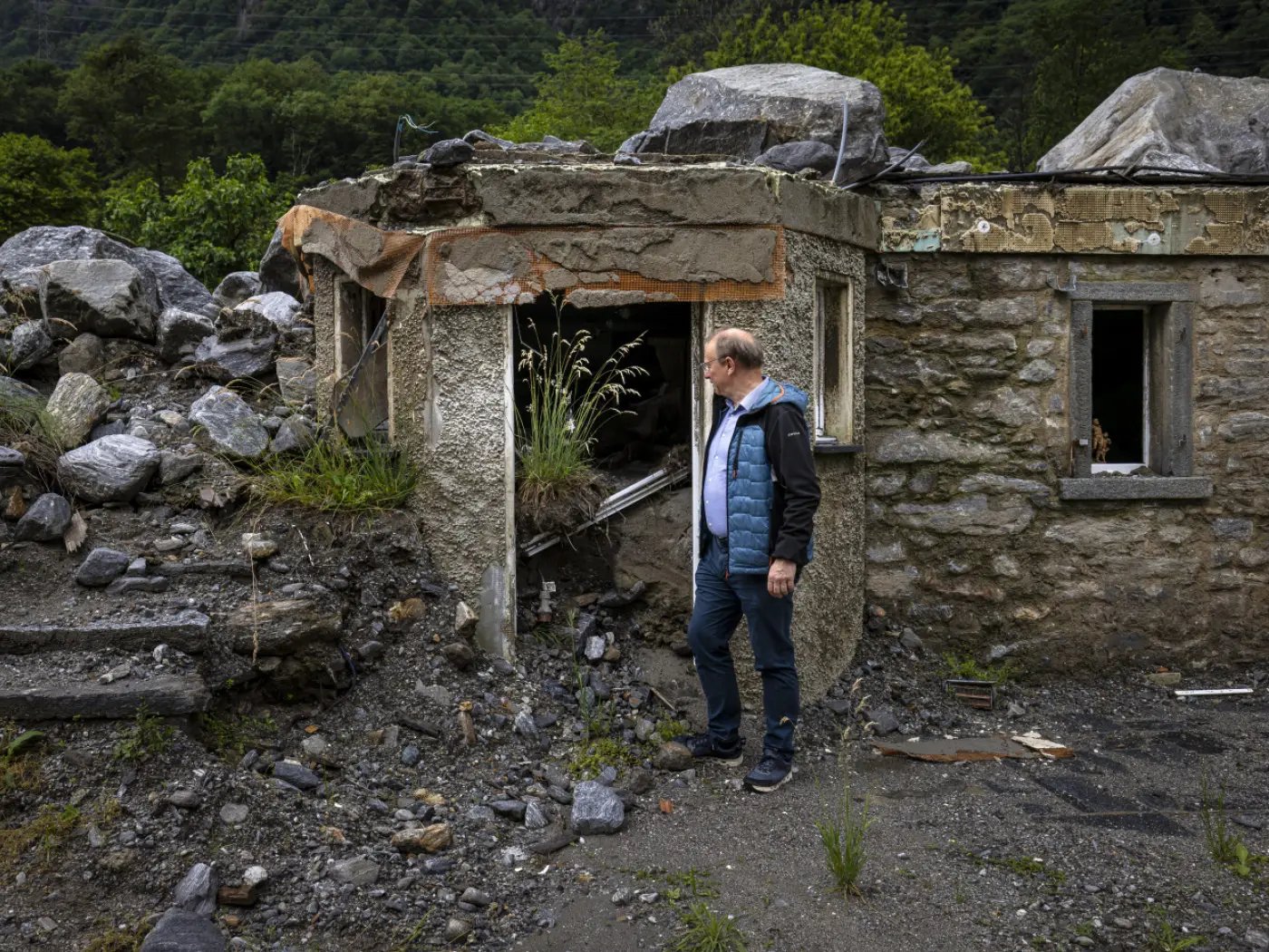 Uomo che osserva un edificio in rovina, con pietre e vegetazione che crescono tra i detriti.