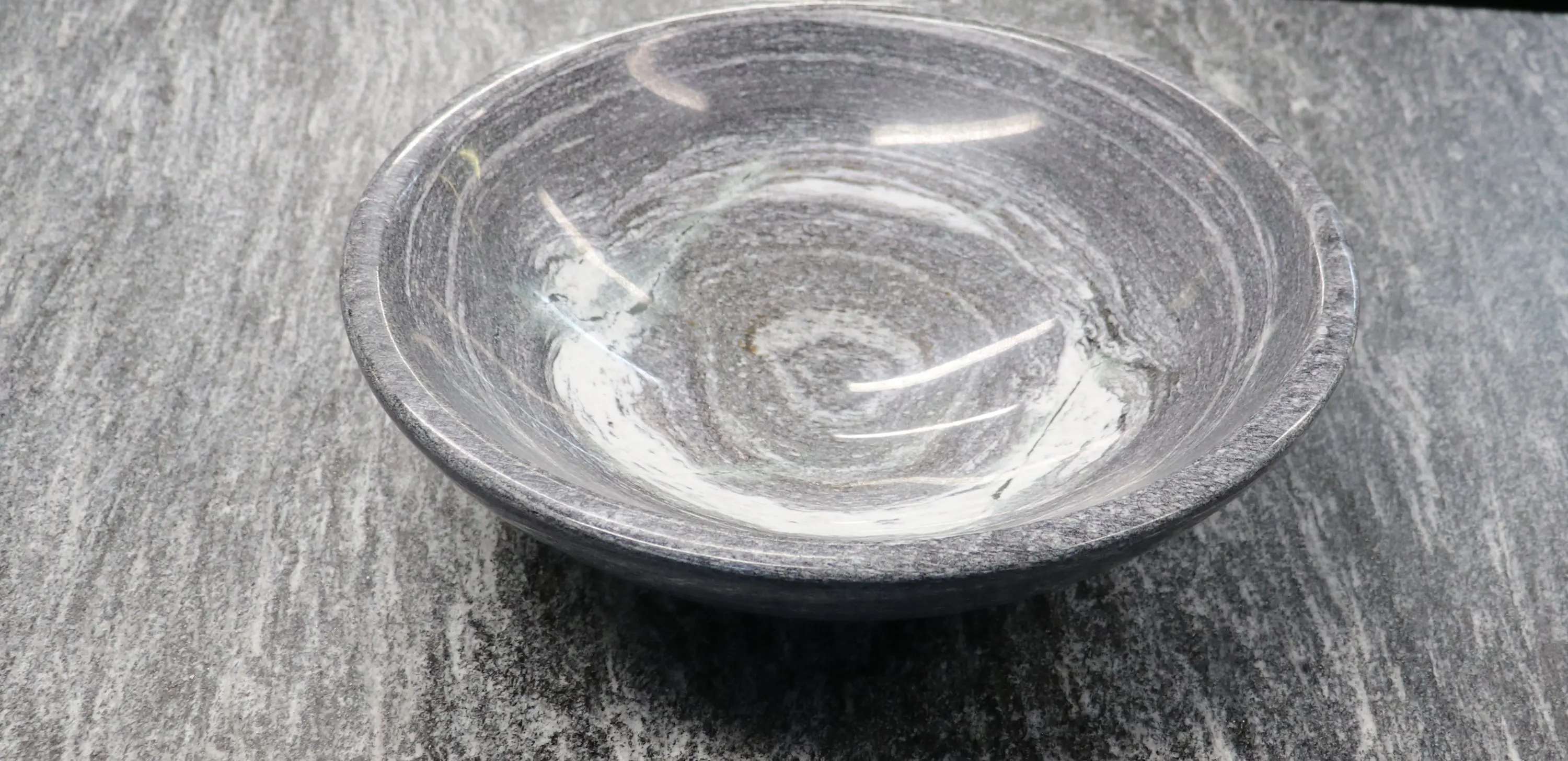 Ciotola di marmo grigio con un design striato. La superficie interna è liscia e lucida, mentre l'esterno presenta una texture più ruvida.