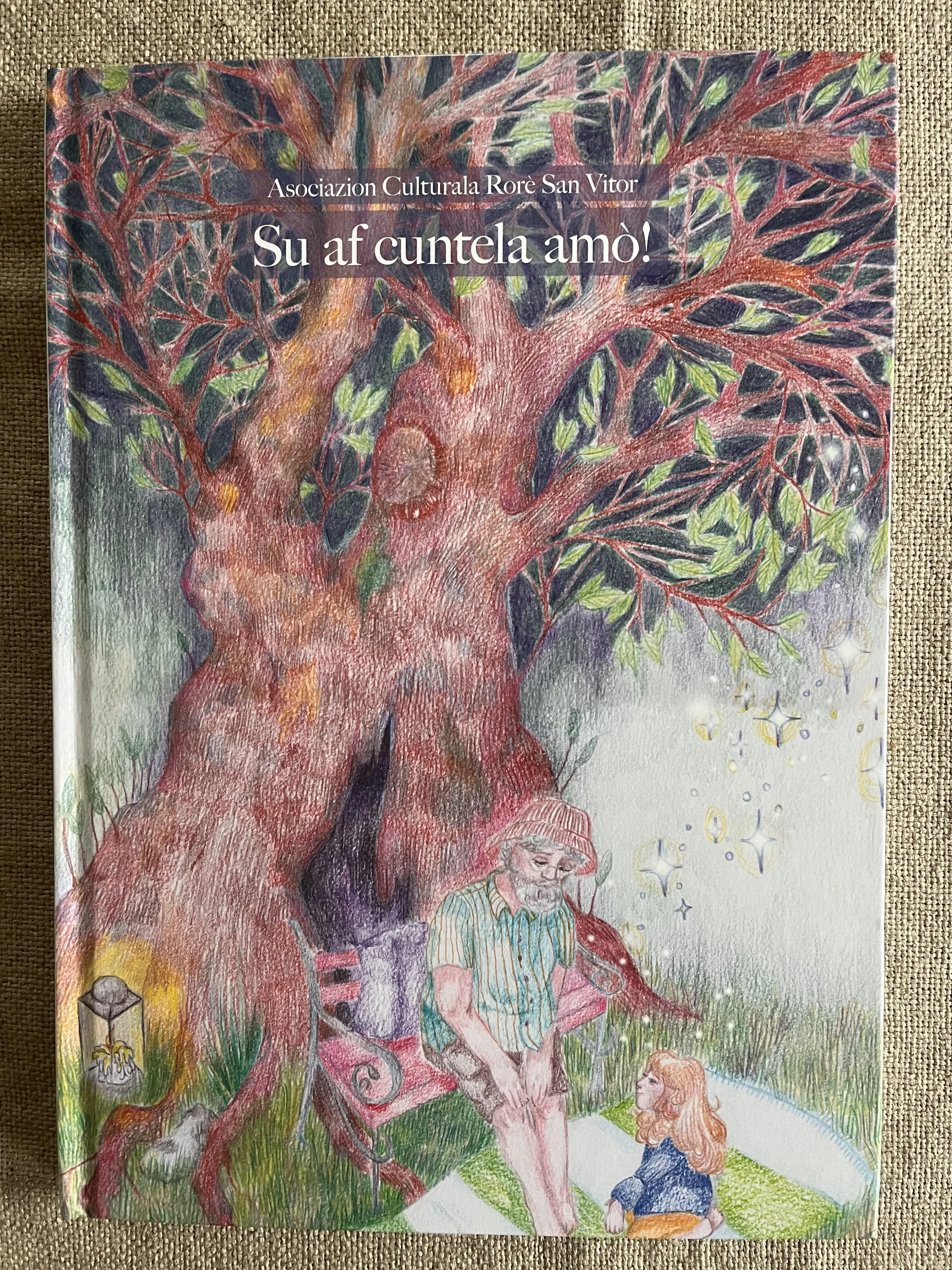 Copertina di un libro con un'illustrazione colorata di un albero grande e ricco di foglie. Un uomo e una donna siedono ai suoi piedi, immersi in una conversazione, mentre un piccolo lume è posizionato accanto a loro.
