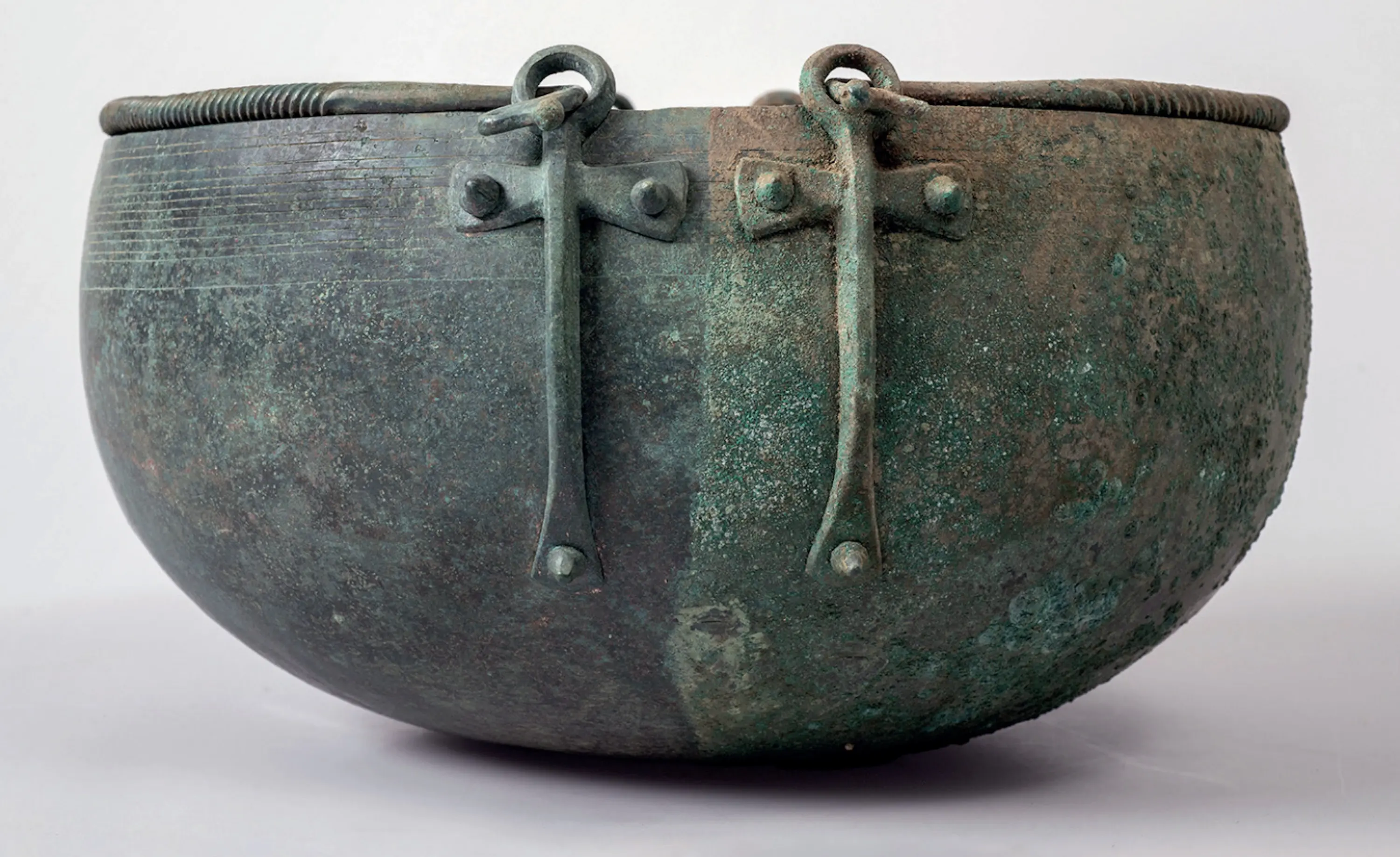 Vasellame in bronzo con una forma semisferica, caratterizzato da maniglie tonde e una superficie verde ossidata.