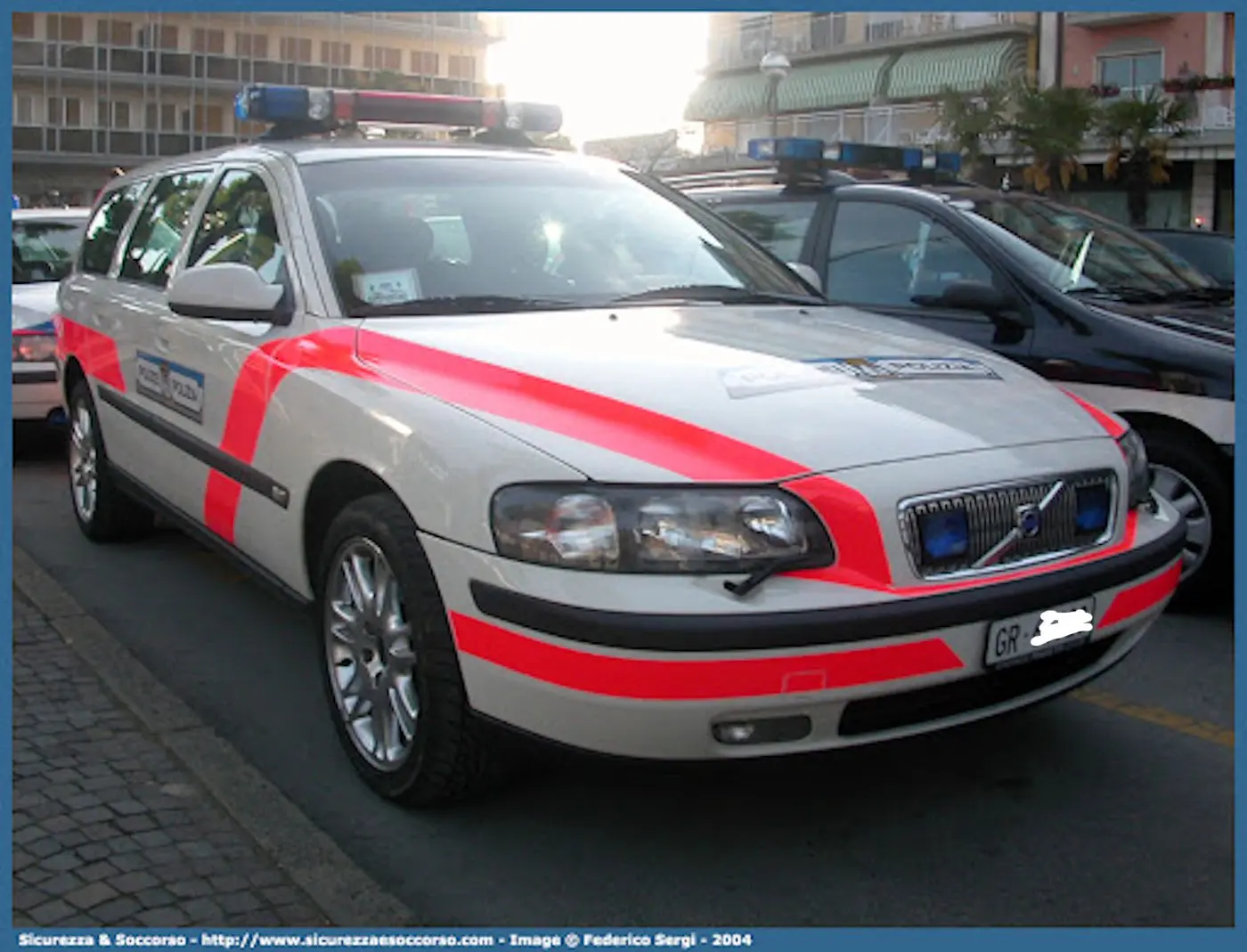 Auto della polizia con strisce rosse e blu, parcheggiata su una strada in città.