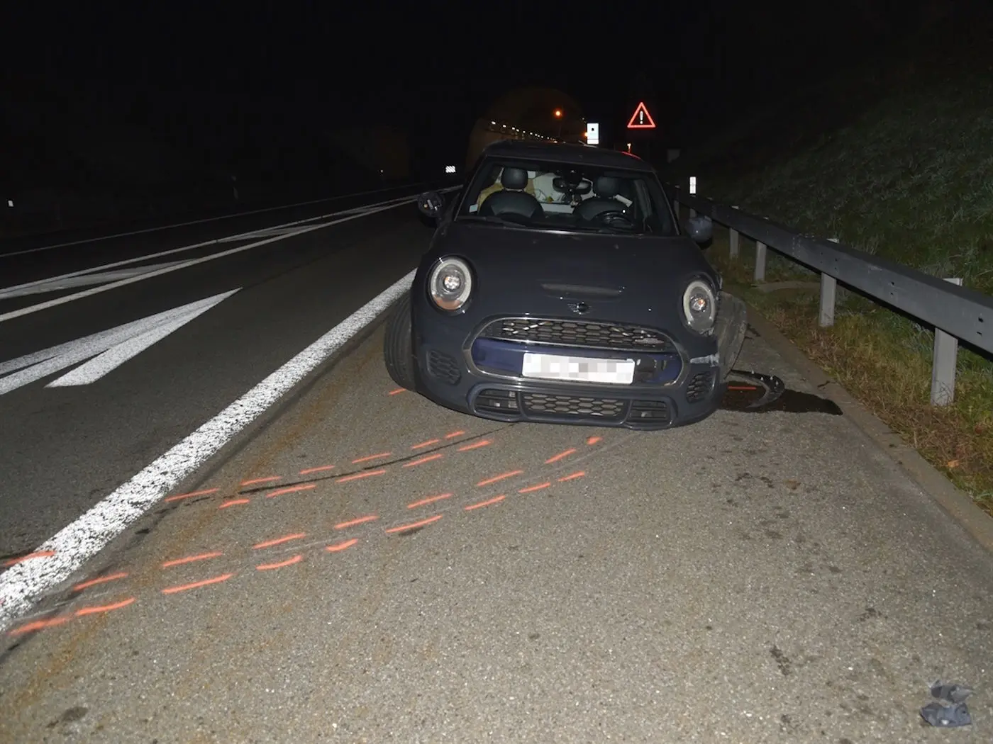 Un'auto nera parcheggiata sul lato di una strada buia, con un segnale di emergenza in lontananza e una curva del tunnel visibile. Tracce rosse evidenziano il percorso dell'auto.