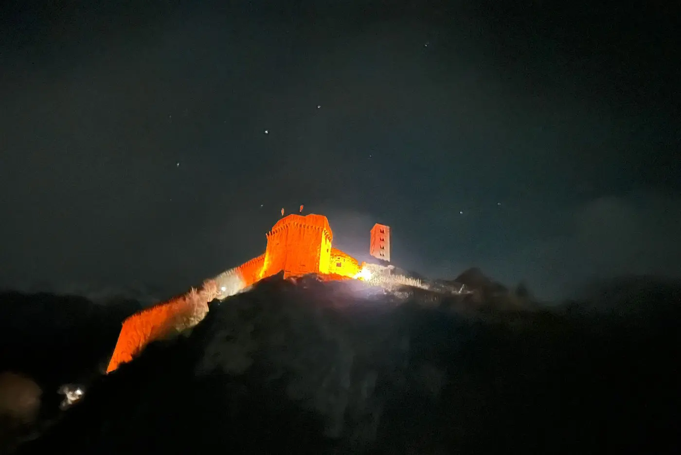 Una fortezza illuminata di arancione su una collina, circondata da un cielo notturno stellato.