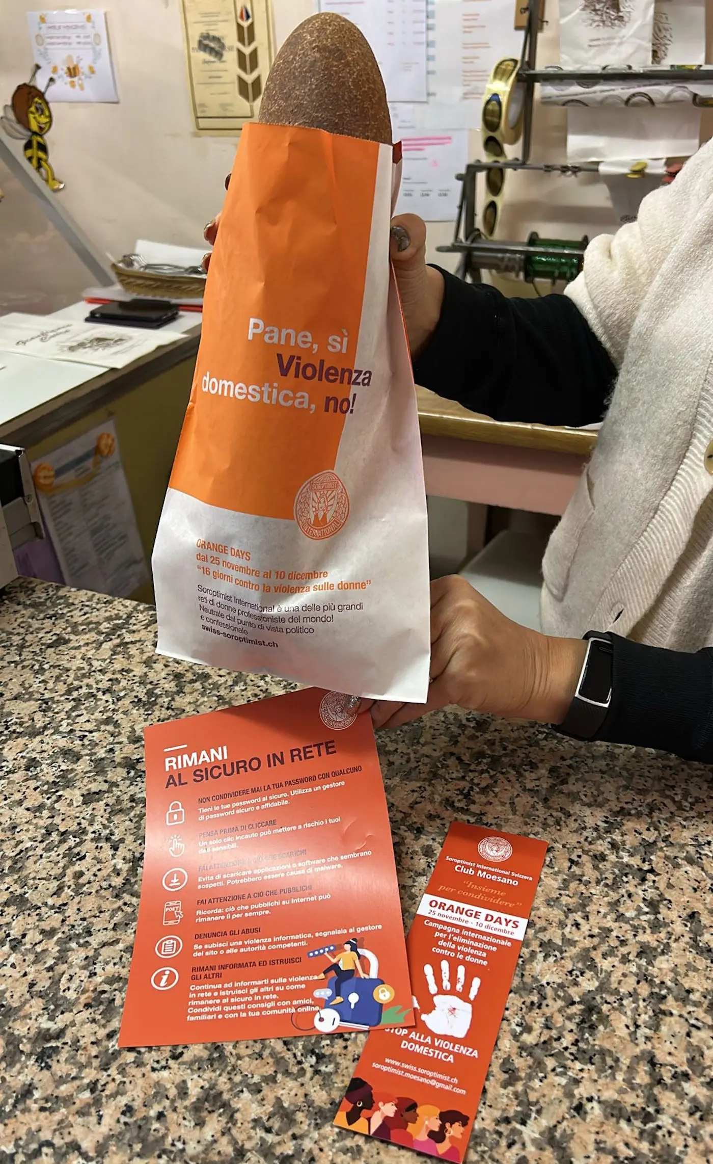Un sacchetto di pane in mano, accanto a fogli informativi che promuovono la sicurezza e la lotta contro la violenza domestica.