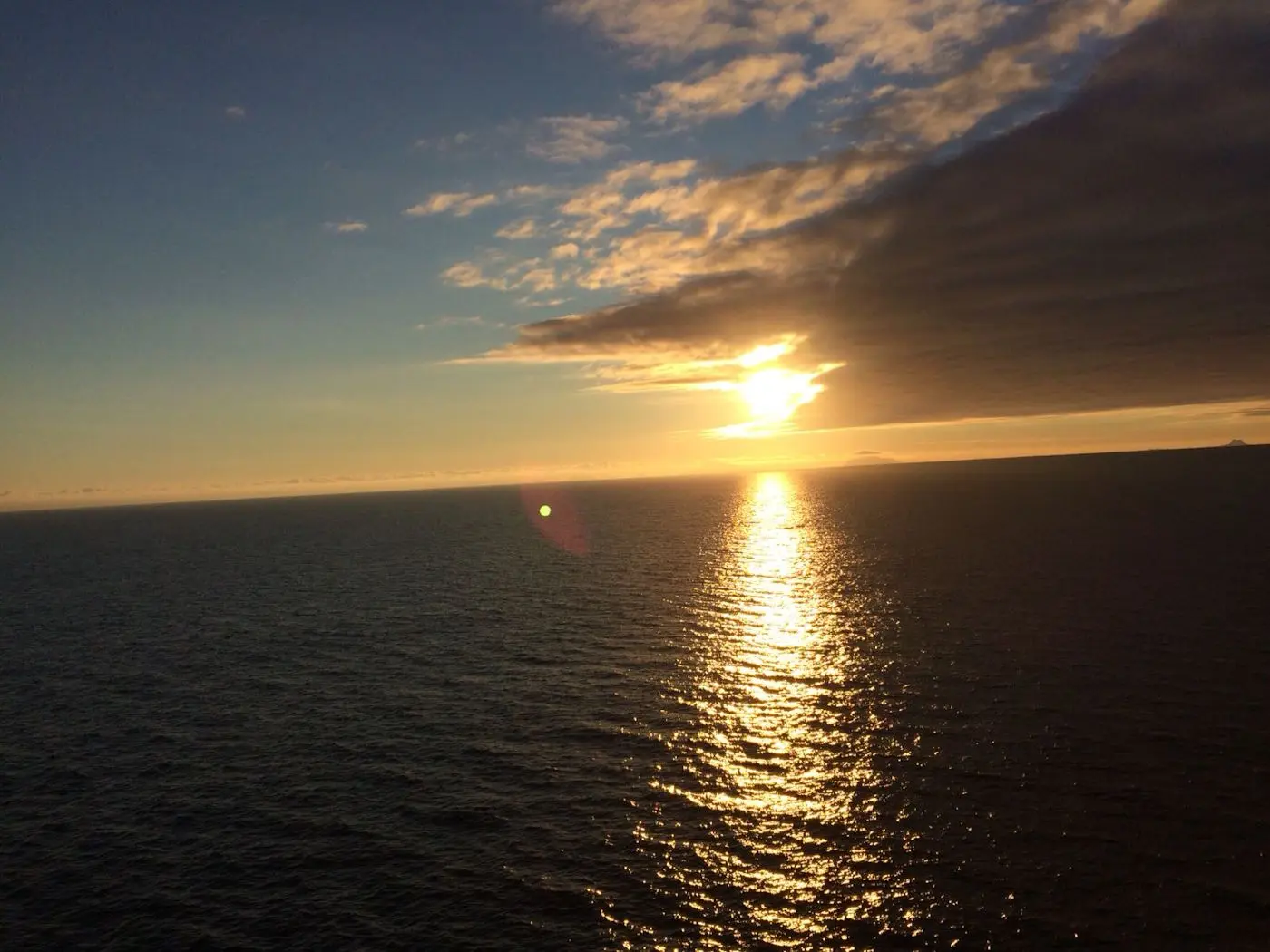 Un tramonto luminoso sul mare, con il sole che si riflette sulle acque e nuvole scure all'orizzonte. Le onde brillano al sole, creando un'atmos