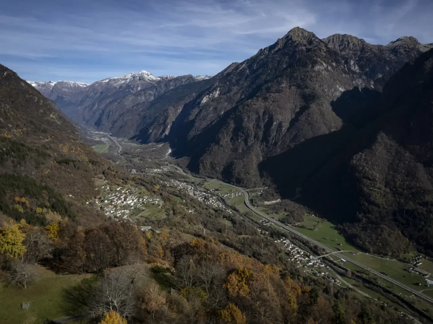 Panorama delle Alpi con valli verdissime e montagne maestose. Ombre profonde si stagliano sulle pendici montane, mentre un fiume scorre lungo la valle.