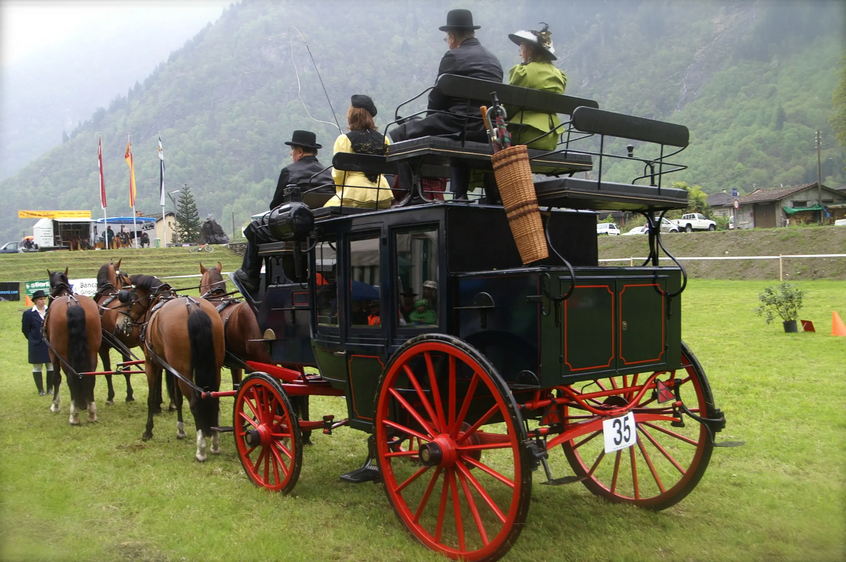 Un'elegante carrozza con ruote rosse, trainata da cavalli, trasporta passeggeri vestiti in abiti storici. Sullo sfondo ci sono bandiere e una zona verde montana.