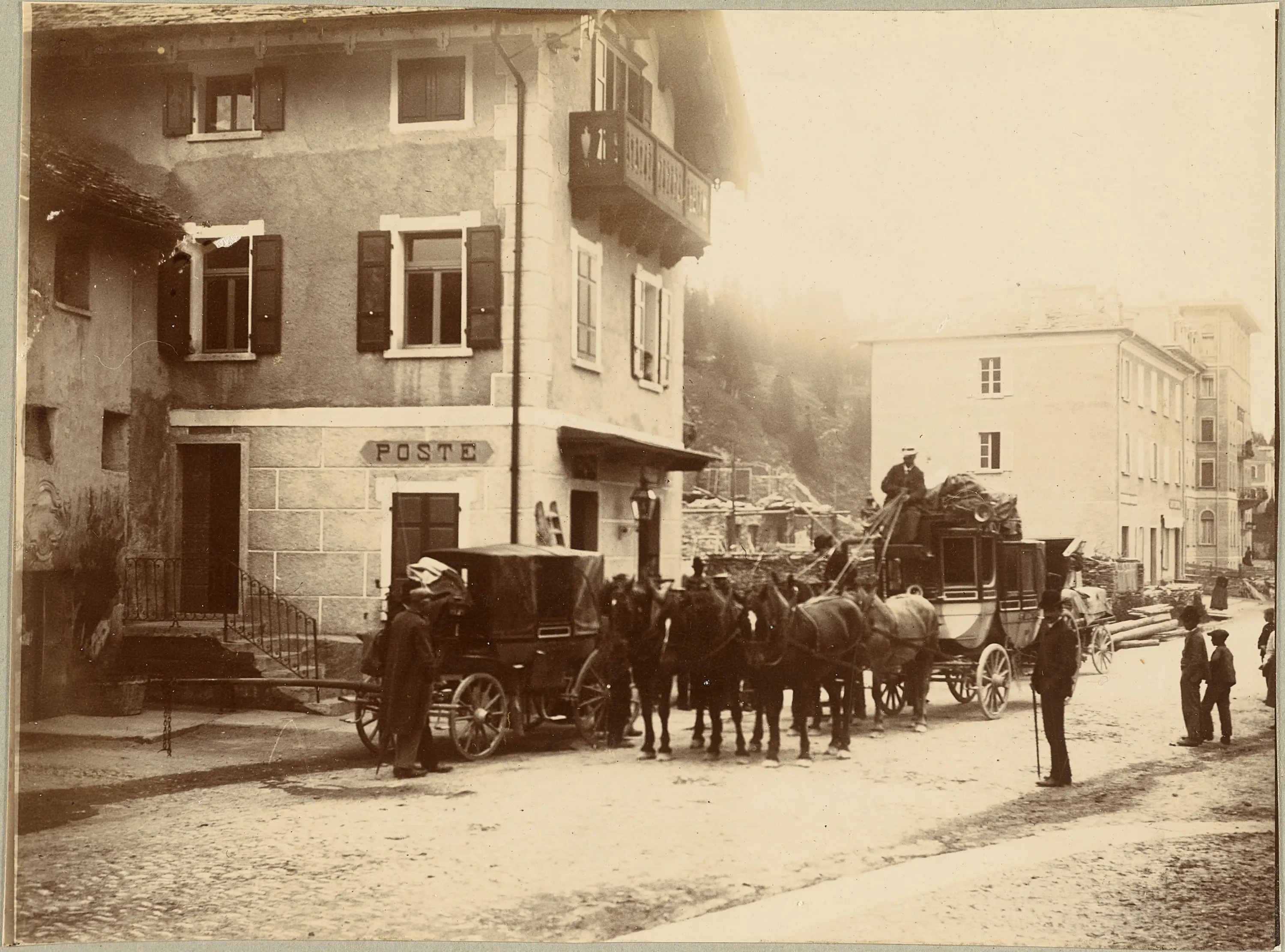 Una scena storica di un villaggio, con un edificio che funge da ufficio postale. Davanti, due carrozze trainate da cavalli sono parcheggiate, mentre alcune persone sono in attesa. Sullo sfondo, si vedono altri edifici e rovine.
